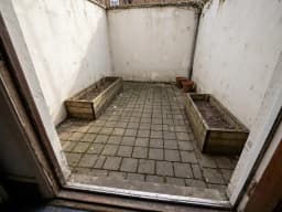 Kleiner gepflasterter Innenhof mit zwei leeren Hochbeeten, vor der Neugestaltung