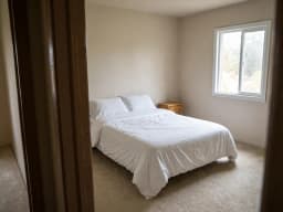Plain bedroom with white bedding and bare walls, before decorating