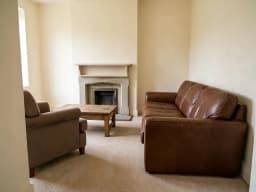 Living room with leather sofas and a fireplace with an empty mantel, before decorating